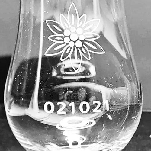 A whisky glass machine engraved with a date and a decorative flower petal design
